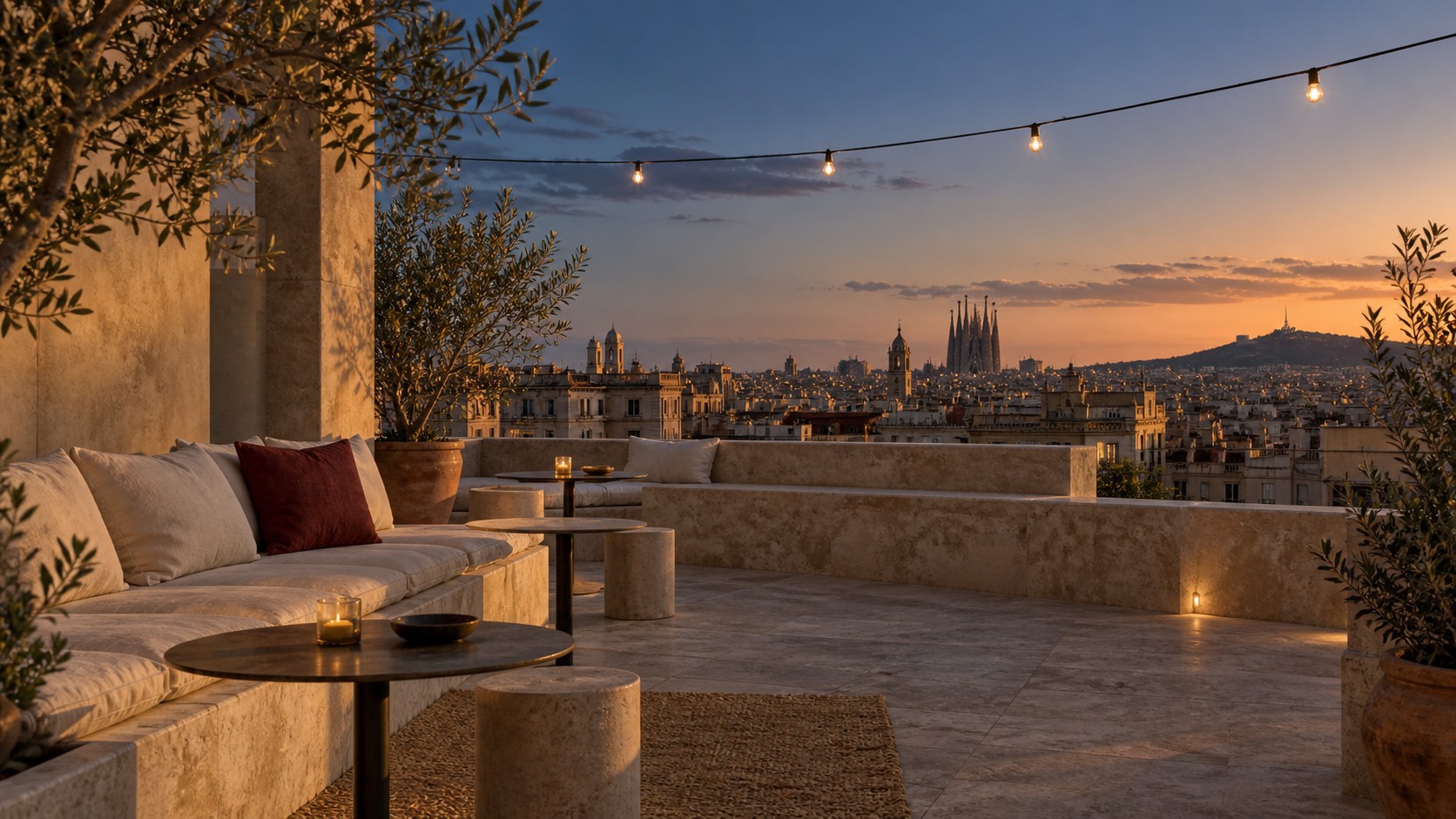 Een leeg dakterras met zachte kussens en lichtslingers boven de daken van Barcelona bij zonsondergang