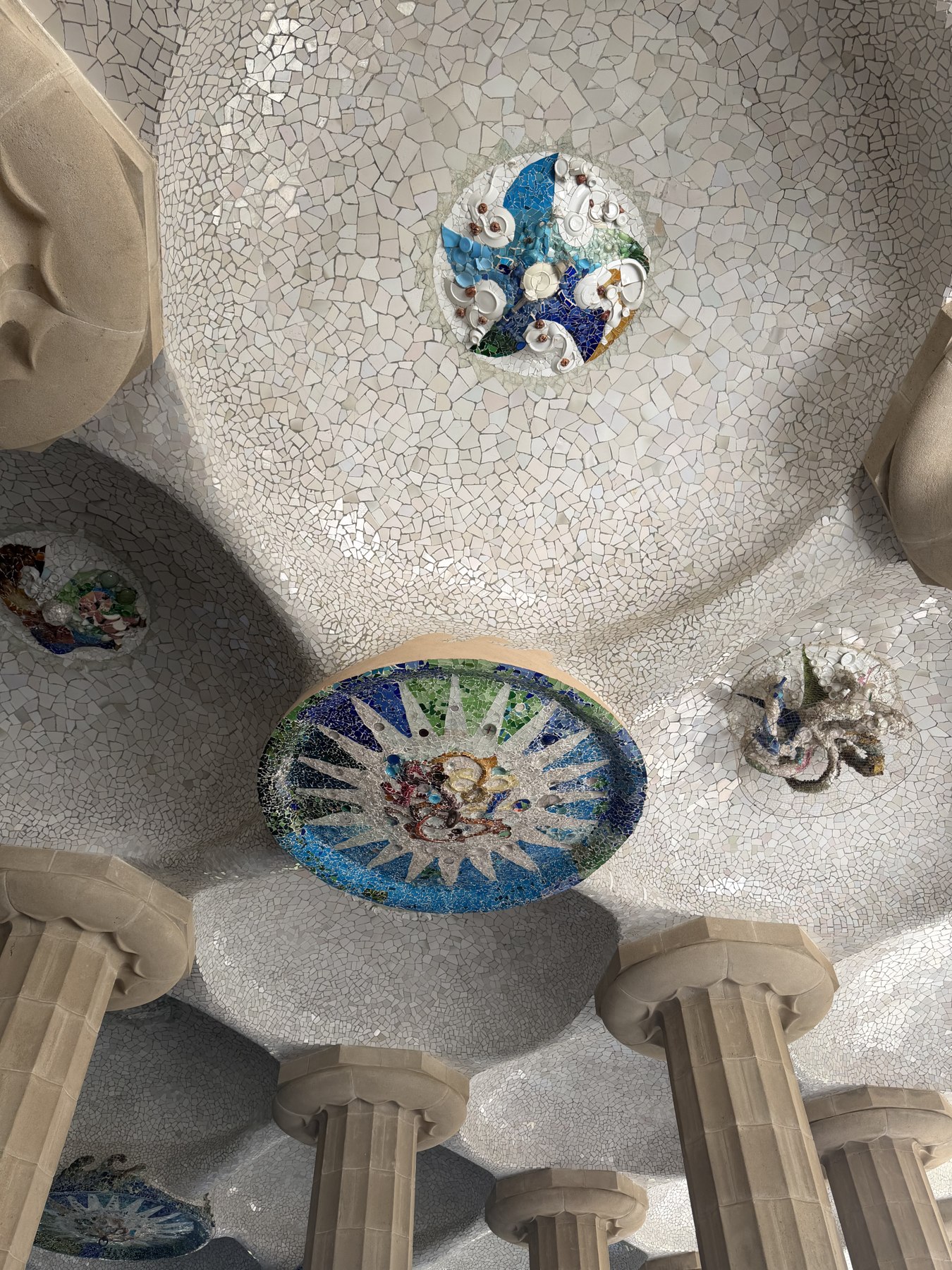Witte mozaïeken, blauwe patronen en zandkleurige zuilen in Park Güell
